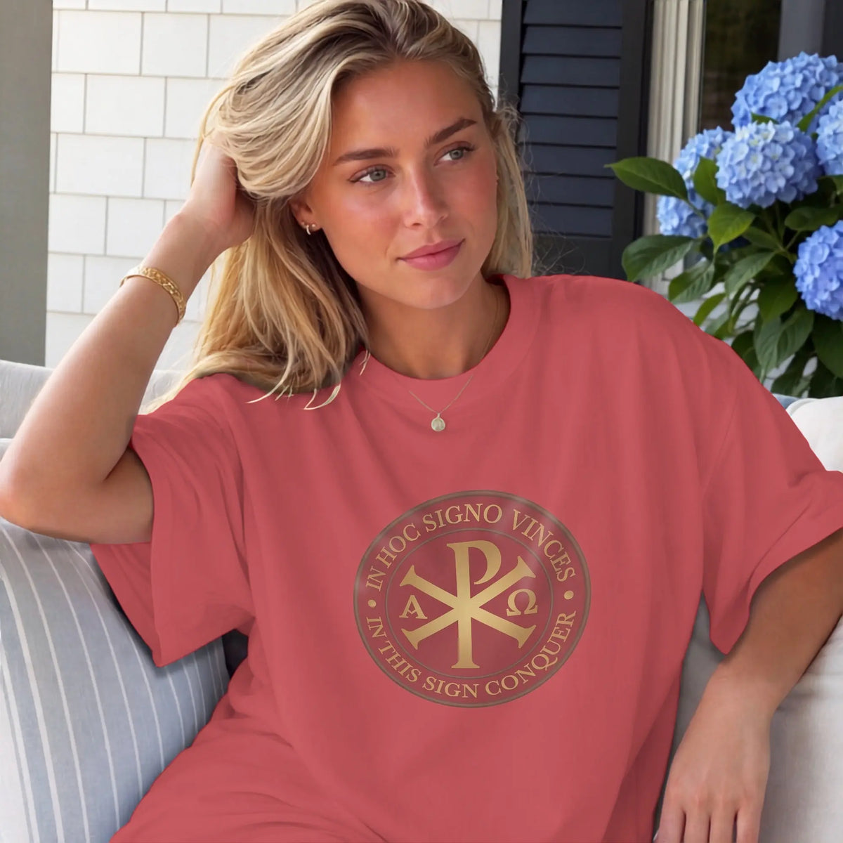 Woman in coral t-shirt with gold Chi-Rho symbol and Latin text.