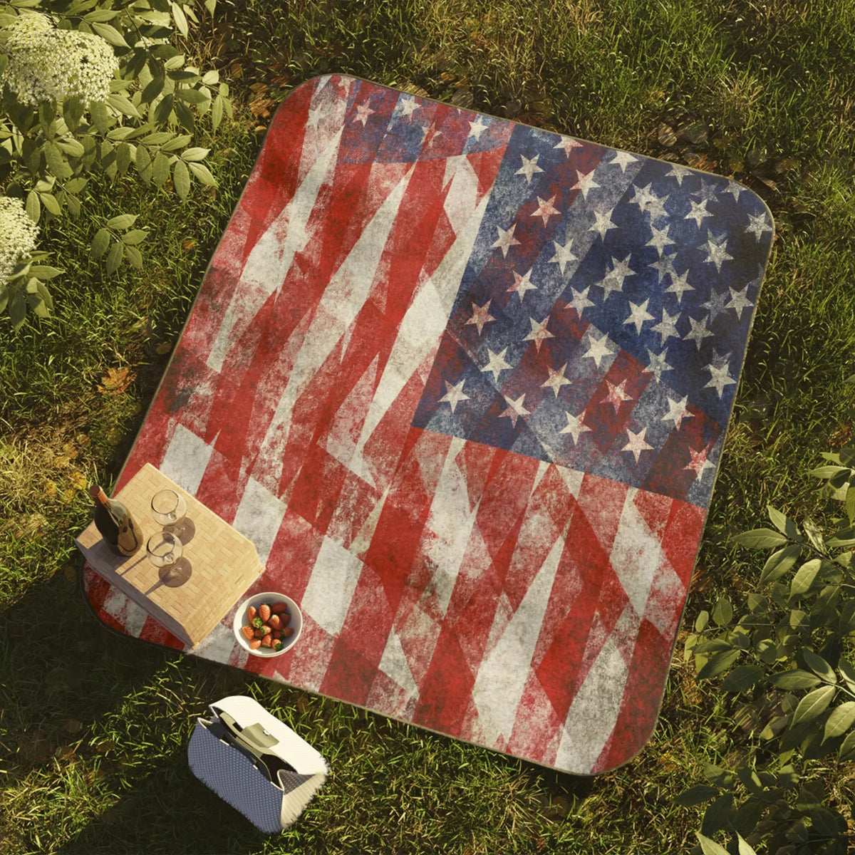 Picnic blanket with distressed American flag design on grass with wine and snacks.